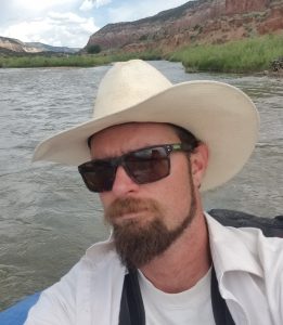 Nathan Oswald in a hat and sunglasses on the river.