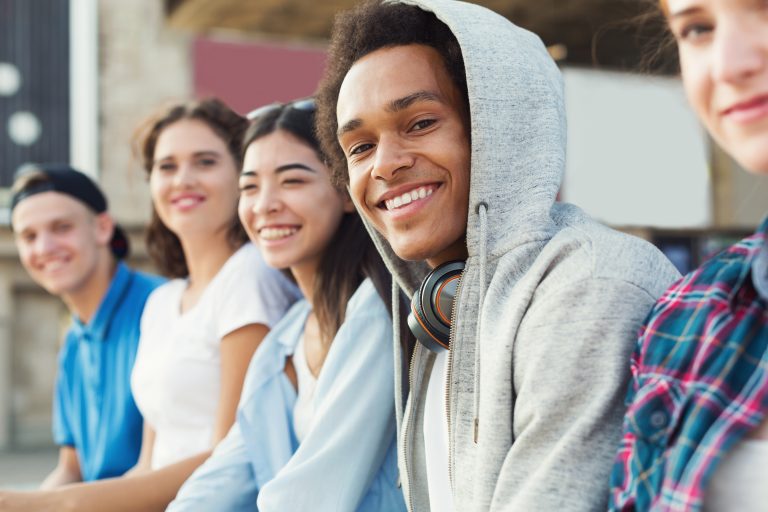 A group of teens smiling at the camera while seated outside.