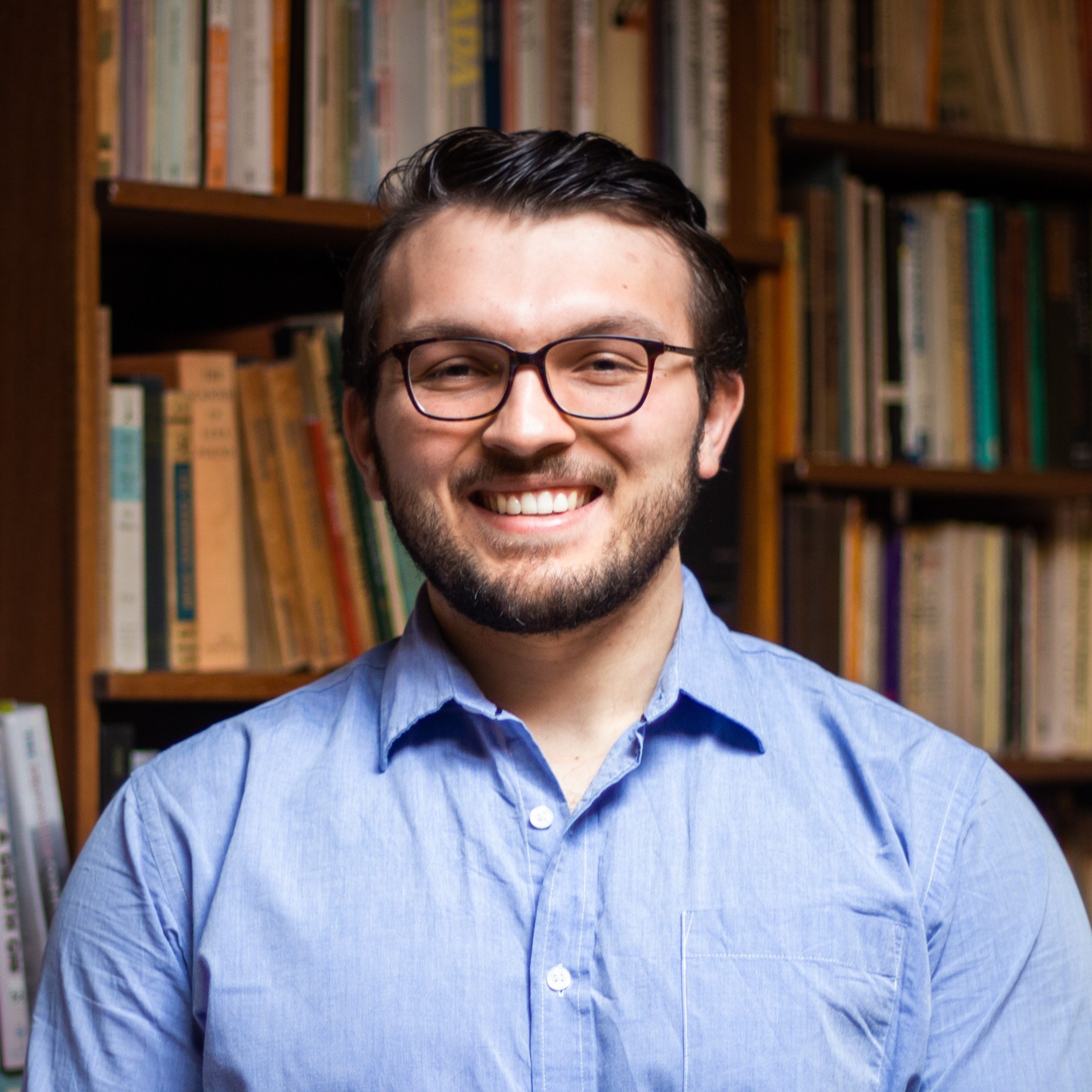 Joshua Rysanek smiles in front of a bookcase